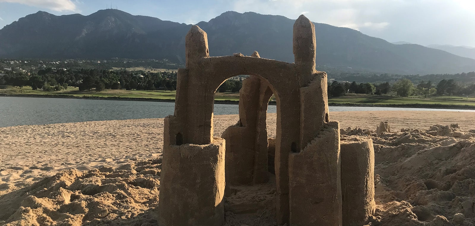 sandcastle by water's edge with mountains in background